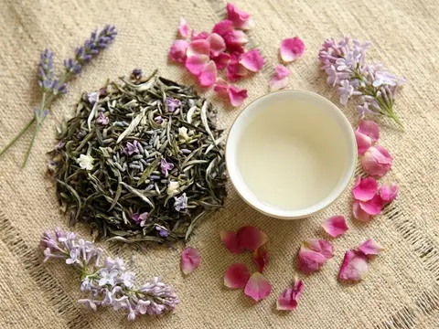 Delicate Buds Designer Tea, handmade Ceylon green tea with lavender and flower petals beside a cup of pale tea